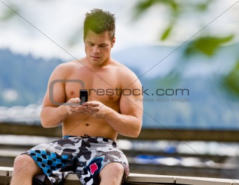 Man sitting on pier text messaging on cell phone