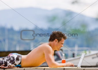Man laying on pier typing on laptop
