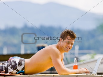 Man laying on pier typing on laptop