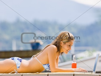 Woman laying on pier typing on laptop