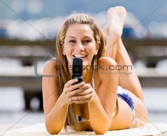 Woman laying on pier text messaging on cell phone