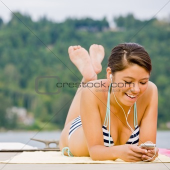 Woman laying on pier listening to mp3 player