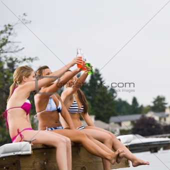 Friends sitting on pier at lake toasting with soda