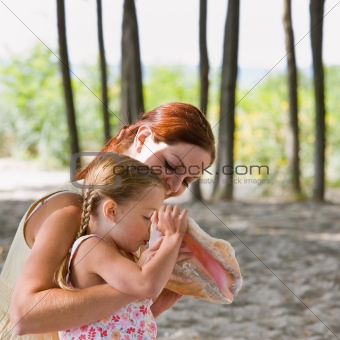 Mother watching daughter blow into seashell