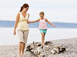 Mother helping daughter walk on log at beach