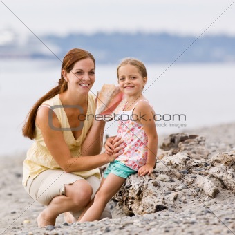Mother and daughter listening to seashell at beach