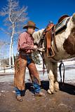 Cowboy Putting Saddle on Horse