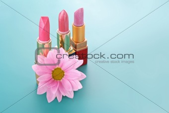 Three new lipsticks and pink flower on blue background