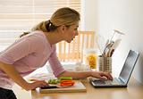 female cooking and looking at laptop in kitchen