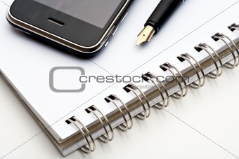 extreme closeup of a fountain pen, spiral notebook and cell phone