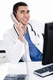 Smiling young physician sitting at his desk talking over phone