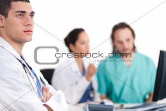 Young doctor thinking deeply, collegues discussing behind with computer
