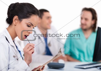 Young asian doctor thinking with the pen, others blurred behind