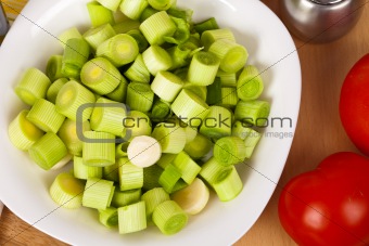 Fresh chopped leeks on a wooden board with red tomatoes