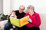 Grandparents reading book to baby girl.
