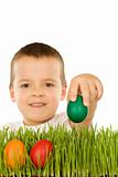 Boy putting colorful easter eggs in the grass