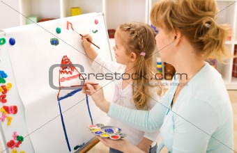 Little girl painting with her mother