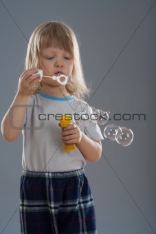 boy with long blond hair looking at big soap bubble - isolated on gray