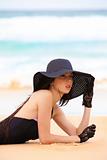 Woman in Black Swimsuit, Hat, and Gloves at the Beach