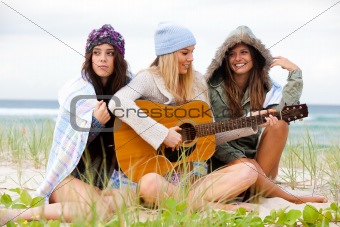 Three Young Women Sitting on Chilly Beach With Guitar