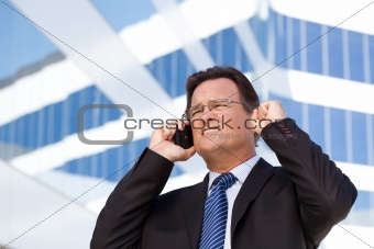 Excited Businessman Using Cell Phone Clinches His Fist in Joy Outside of Corporate Building.