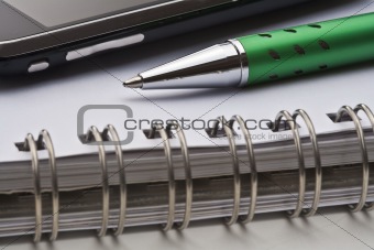 extreme closeup of a ballpoint pen, spiral notebook and cell phone