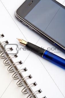 closeup of a fountain pen, spiral notebook and cell phone