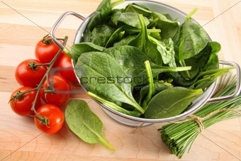 Strainer with spinach leaves and tomatoes