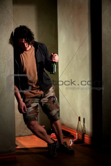 Drunk young man leaning on a wall with beer bottle