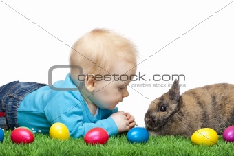 Male young Baby sitting in meadow together with Easter bunny and colorful eggs.