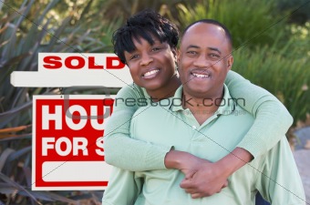 Happy African American Couple in Front of Sold Home For Sale Real Estate Sign.