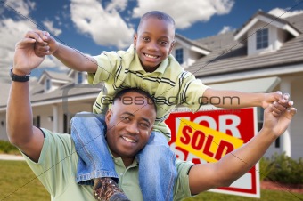 Happy African American Father and Son in Front of New Home and Sold Real Estate Sign.