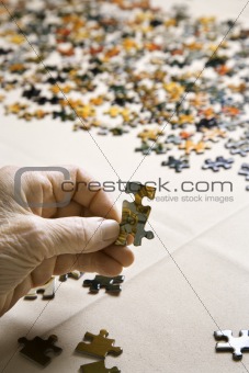 Elderly Caucasian woman's hand holding puzzle piece. 