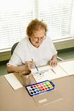 Elderly Caucasian woman painting with watercolors.