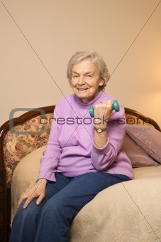 Elderly Caucasian woman lifting weights on bed.