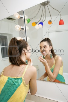 Young female looking in mirror applying makeup.