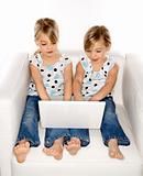 Female children twins playing with laptop computer.