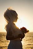 Bride at sunset holding bouquet on beach.