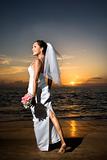 Bride standing holding bouquet on beach.