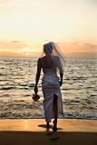 Bride standing on beach at sunset.
