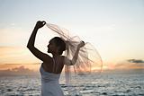 Bride holding out veil on beach.