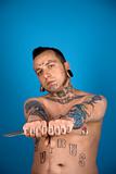 Adult male with tattoos and piercings holding knife.