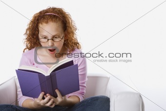 Girl sitting reading book looking surprised.