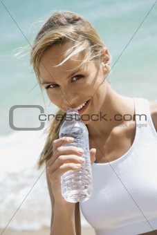 Woman drinking water on beach.