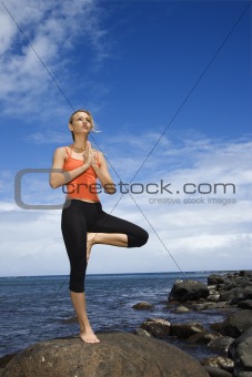 Woman doing yoga on rocky shore.