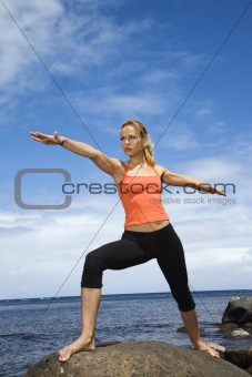 Woman doing yoga on rocky shore.