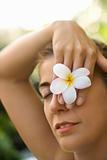 Woman holding plumeria flower over eye.