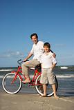 Father on bike with arm around son on beach. 