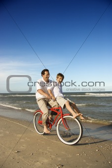 Dad riding red bicycle with son on handlebars. 