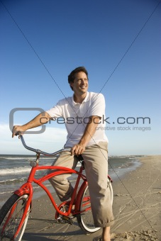 Mid-adult man riding red bicycle on beach.